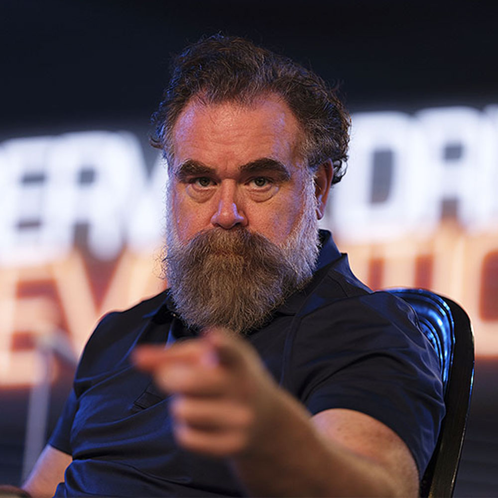 pointing directly at the camera while sitting in a studio setting.